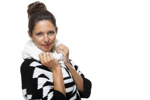 Attractive elegant woman in winter fashion snuggling down into her white scarf and black and white jumper to ward off the cold winter weather, on white