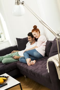 Happy Young Sweet Couple in Casual Clothing Smiling at Each Other While Sitting at the Couch in the Living Room