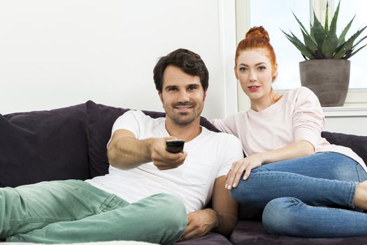 Happy Young Sweet Couple in Casual Clothing Smiling at Each Other While Sitting at the Couch in the Living Room