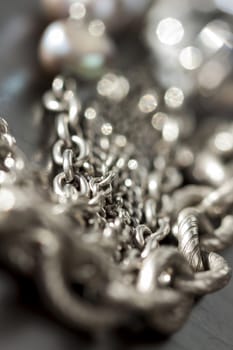 Assorted silver costume jewellery with a jumbled pile of chains with different shaped links, a clear crystal bead and a necklace of round silver beads with focus to the chains