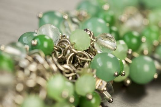 Close up view of pretty translucent green beads on an item of silver jewellery attached in a bunch to a ring by short chains with shallow dof in a fashion concept