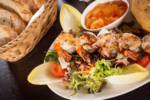 Grilled prawns with a green leafy lettuce and endive salad and a jacket potato topped with sour cream served on a white plate, close up high angle view on white
