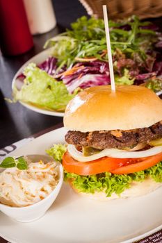 Tasty traditional cheeseburger with a ground beef patty topped with melted cheese and served with onion rings, tomato and curly leaf lettuce on a round white bread roll, close up view