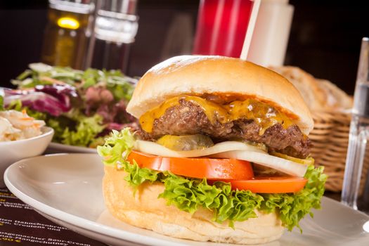 Tasty traditional cheeseburger with a ground beef patty topped with melted cheese and served with onion rings, tomato and curly leaf lettuce on a round white bread roll, close up view