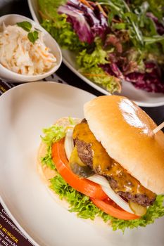 Tasty traditional cheeseburger with a ground beef patty topped with melted cheese and served with onion rings, tomato and curly leaf lettuce on a round white bread roll, close up view