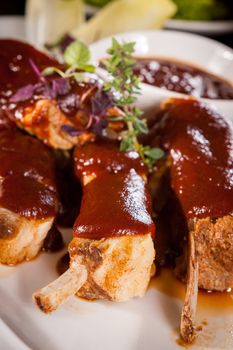 Delicious grilled pork ribs served with a rich brown gravy or BBQ sauce garnished with fresh herbs , close up side view