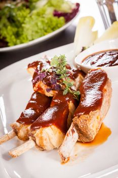 Delicious grilled pork ribs served with a rich brown gravy or BBQ sauce garnished with fresh herbs , close up side view