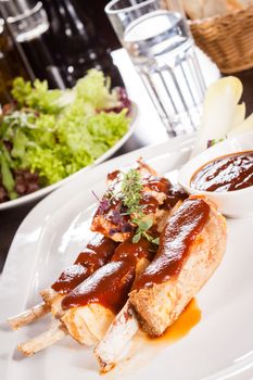 Delicious grilled pork ribs served with a rich brown gravy or BBQ sauce garnished with fresh herbs , close up side view