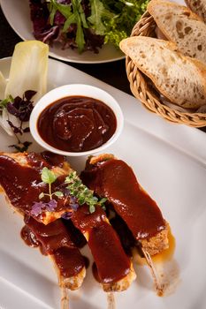 Delicious grilled pork ribs served with a rich brown gravy or BBQ sauce garnished with fresh herbs , close up side view