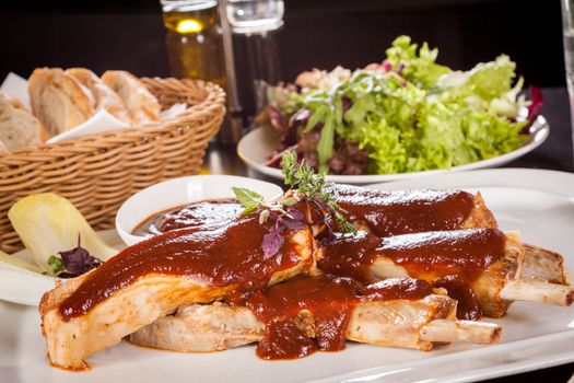 Delicious grilled pork ribs served with a rich brown gravy or BBQ sauce garnished with fresh herbs , close up side view