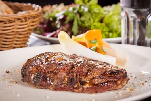 Delicious trimmed lean portion of thick grilled beef steak with seasoning served on a white plate, close up with shallow dof