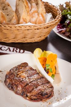 Delicious trimmed lean portion of thick grilled beef steak with seasoning served on a white plate, close up with shallow dof