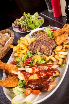 Wholesome platter of mixed meats including grilled steak, crispy crumbed chicken and beef on a bed of fresh leafy green mixed salad served with French fries and chutney or BBQ sauce in a dish