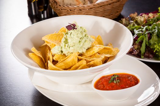 Crisp corn nachos with spicy fresh guacamole sauce and a topping of avocado served as a snack or appetizer in a white bowl