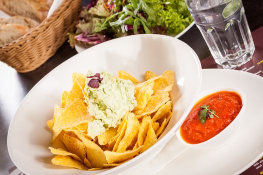 Crisp corn nachos with spicy fresh guacamole sauce and a topping of avocado served as a snack or appetizer in a white bowl