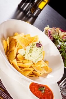 Crisp corn nachos with spicy fresh guacamole sauce and a topping of avocado served as a snack or appetizer in a white bowl