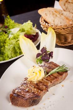 Tasty grilled beef steak topped with a twirled knob of butter and a sprig of fresh rosemary and served on a white plate, close up view