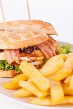 Club sandwich on toasted white bread with a meat filling served with crispy golden potato French fries, closeup partial view isolated on white