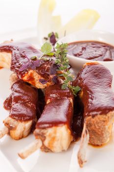 Delicious grilled pork ribs served with a rich brown gravy or BBQ sauce garnished with fresh herbs , close up side view