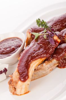 Delicious grilled pork ribs served with a rich brown gravy or BBQ sauce garnished with fresh herbs , close up side view