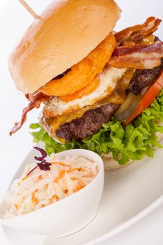 Delicious egg and bacon cheeseburger with a nutritional filling of salad ingredients, a ground beef patty, cheese, fried egg and crispy bacon on a white crusty roll