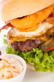 Delicious egg and bacon cheeseburger with a nutritional filling of salad ingredients, a ground beef patty, cheese, fried egg and crispy bacon on a white crusty roll