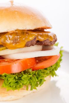 Tasty traditional cheeseburger with a ground beef patty topped with melted cheese and served with onion rings, tomato and curly leaf lettuce on a round white bread roll, close up view