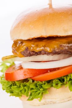 Tasty traditional cheeseburger with a ground beef patty topped with melted cheese and served with onion rings, tomato and curly leaf lettuce on a round white bread roll, close up view