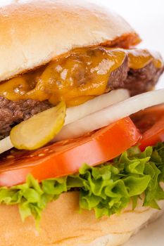 Tasty traditional cheeseburger with a ground beef patty topped with melted cheese and served with onion rings, tomato and curly leaf lettuce on a round white bread roll, close up view