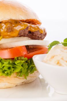 Tasty traditional cheeseburger with a ground beef patty topped with melted cheese and served with onion rings, tomato and curly leaf lettuce on a round white bread roll, close up view