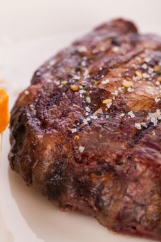 Delicious trimmed lean portion of thick grilled beef steak with seasoning served on a white plate, close up with shallow dof