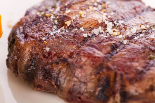 Delicious trimmed lean portion of thick grilled beef steak with seasoning served on a white plate, close up with shallow dof