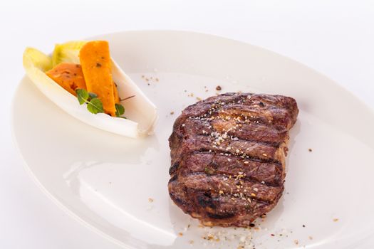 Delicious trimmed lean portion of thick grilled beef steak with seasoning served on a white plate, close up with shallow dof