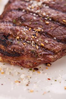 Delicious trimmed lean portion of thick grilled beef steak with seasoning served on a white plate, close up with shallow dof