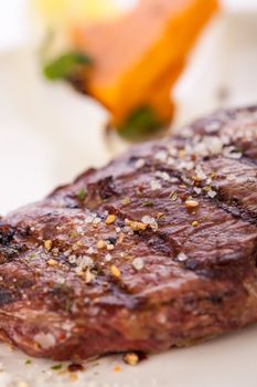 Delicious trimmed lean portion of thick grilled beef steak with seasoning served on a white plate, close up with shallow dof