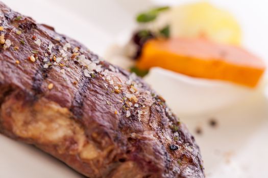 Delicious trimmed lean portion of thick grilled beef steak with seasoning served on a white plate, close up with shallow dof