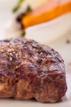 Delicious trimmed lean portion of thick grilled beef steak with seasoning served on a white plate, close up with shallow dof