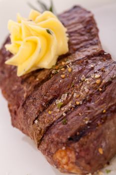 Tasty grilled beef steak topped with a twirled knob of butter and a sprig of fresh rosemary and served on a white plate, close up view