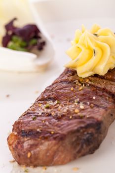 Tasty grilled beef steak topped with a twirled knob of butter and a sprig of fresh rosemary and served on a white plate, close up view