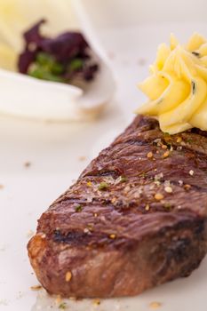 Tasty grilled beef steak topped with a twirled knob of butter and a sprig of fresh rosemary and served on a white plate, close up view