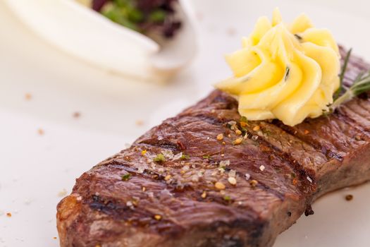 Tasty grilled beef steak topped with a twirled knob of butter and a sprig of fresh rosemary and served on a white plate, close up view