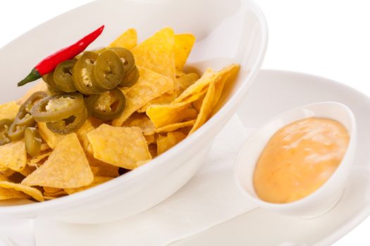 Bowl of crisp golden corn nachos with cheese sauce or dip and olives served as a starter or appetizer to a meal