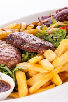 Wholesome platter of mixed meats including grilled steak, crispy crumbed chicken and beef on a bed of fresh leafy green mixed salad served with French fries and chutney or BBQ sauce in a dish