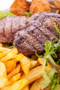 Wholesome platter of mixed meats including grilled steak, crispy crumbed chicken and beef on a bed of fresh leafy green mixed salad served with French fries and chutney or BBQ sauce in a dish