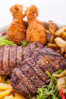 Wholesome platter of mixed meats including grilled steak, crispy crumbed chicken and beef on a bed of fresh leafy green mixed salad served with French fries and chutney or BBQ sauce in a dish