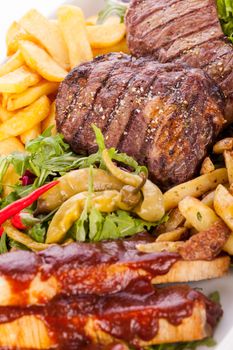 Wholesome platter of mixed meats including grilled steak, crispy crumbed chicken and beef on a bed of fresh leafy green mixed salad served with French fries and chutney or BBQ sauce in a dish