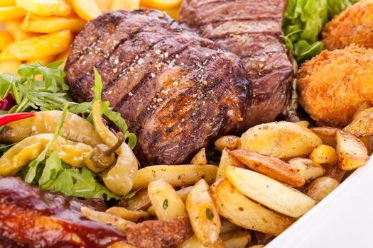 Wholesome platter of mixed meats including grilled steak, crispy crumbed chicken and beef on a bed of fresh leafy green mixed salad served with French fries and chutney or BBQ sauce in a dish