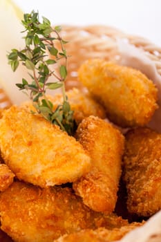 Crispy fried crumbed chicken nuggets in a wicker basket served as a finger food or appetizer with a creamy dip in a bowl alongside