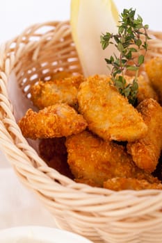 Crispy fried crumbed chicken nuggets in a wicker basket served as a finger food or appetizer with a creamy dip in a bowl alongside