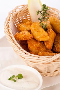 Crispy fried crumbed chicken nuggets in a wicker basket served as a finger food or appetizer with a creamy dip in a bowl alongside